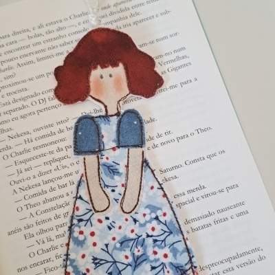 Marcador de livros em forma de boneca de tecido colorido sobre livro aberto
