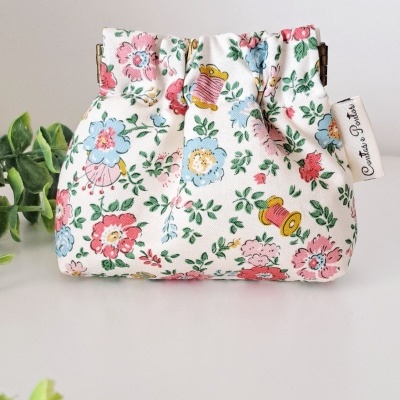 Bolsa de tecido branco com padrão floral e bobinas de linha coloridas.