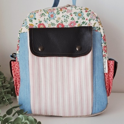 Mochila colorida com padrão floral e bolso de couro preto sobre superfície branca.