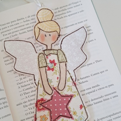 Marcador de livro anjo de tecido com vestido floral e asas brancas sobre livro aberto