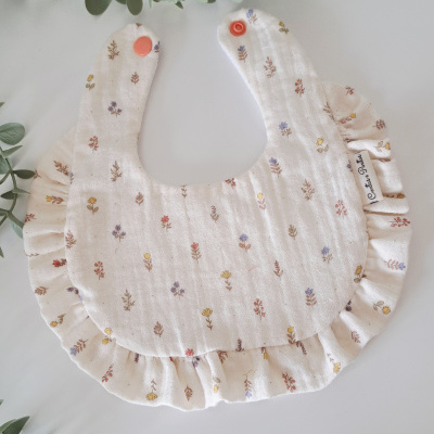 Babete de tecido branco com padrão floral e botões laranja
