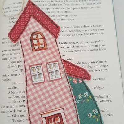 Marcador de livros em forma de casa com padrão xadrez e floral sobre livro aberto