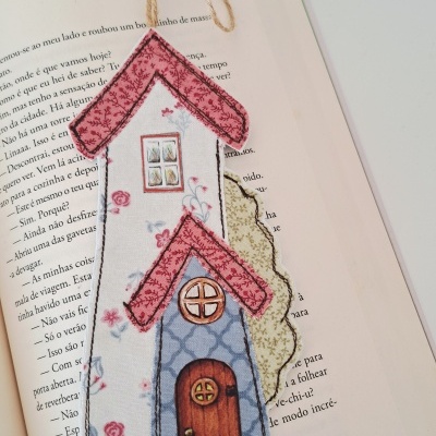 Marcador de livros em tecido em forma de casa sobre livro aberto.