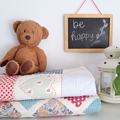 Dois cobertores coloridos, urso de peluche, lanterna branca e quadro-negro com 'be happy'