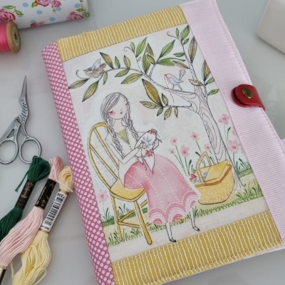 Capa de tecido ilustrada com mulher e plantas, fios de bordar e tesoura