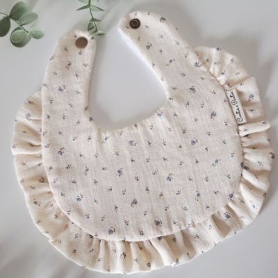 Babete de tecido creme com padrão floral azul e babados nas bordas