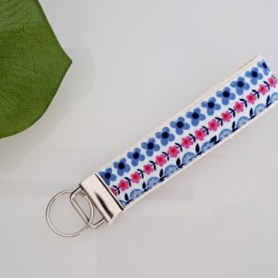 Chaveiro de tecido com padrão floral azul e rosa com argolas metálicas sobre superfície branca