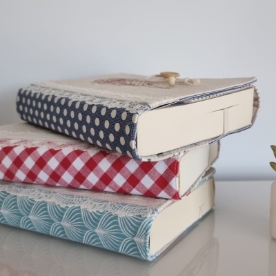 Três livros com capas de tecido decorativo empilhados junto a uma planta suculenta em vaso branco