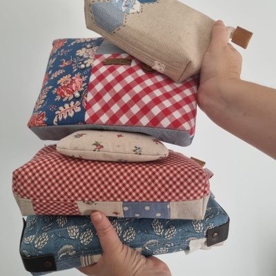 Quatro almofadas decorativas com padrões florais, xadrez e patchwork em azul, vermelho e bege