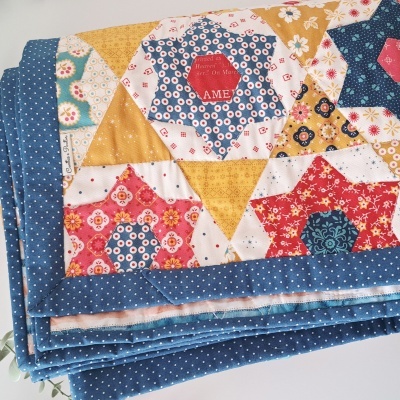 Colcha dobrada com padrão de estrelas coloridas e borda azul de pontos brancos