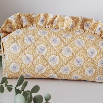 Necessaire acolchoada amarela com padrão floral branco e lilás e babado no topo