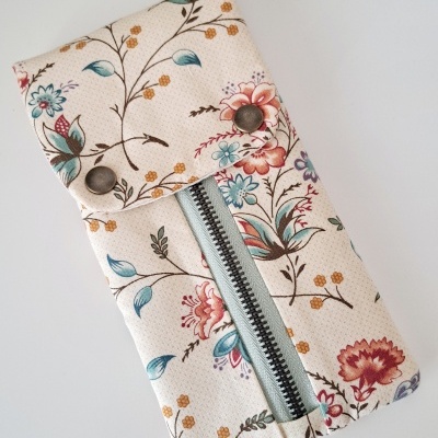 Estojo floral de tecido com fecho e botões sobre mesa branca com flores secas