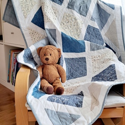 Manta patchwork azul e branca com urso de peluche numa cadeira de madeira