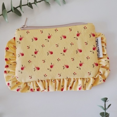 Mala amarela com padrão floral, fecho de correr e babados em fundo branco com ramos verdes