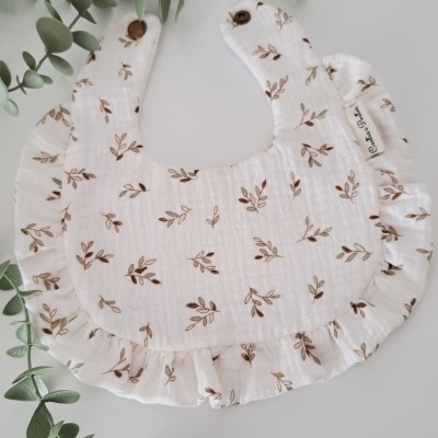 Babete branco com folhas castanhas e folhos, com ramo de folhas verdes ao lado