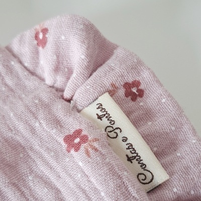 tecido rosa claro com flores vermelhas e etiqueta com texto em fonte cursiva