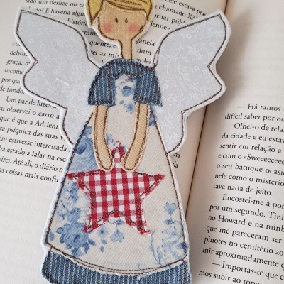 Marcador de páginas de anjo em tecido com vestido azul e estrela vermelha, colocado em livro aberto