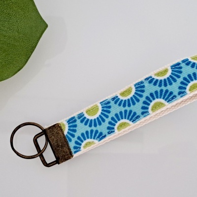 Chaveiro de tecido azul, verde e branco com argola de metal sobre superfície branca