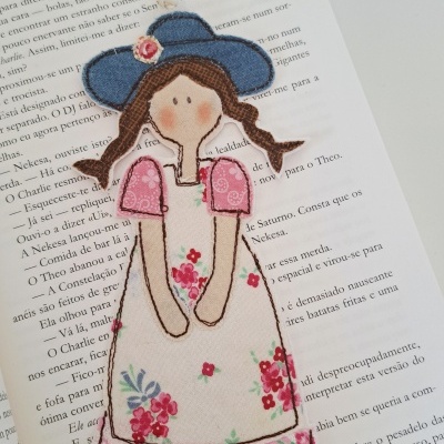 Marcador de livro tecido boneca com vestido floral sobre livro aberto