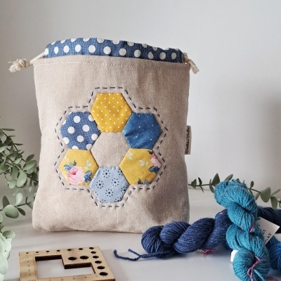 Bolsa artesanal de tecido bege com aplicação hexagonal colorida e novelos de lã
