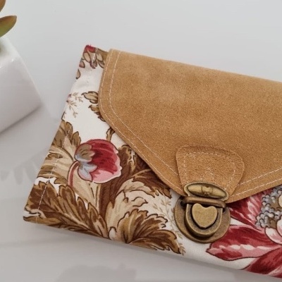 Carteira com padrão floral e fecho metálico ao lado de planta suculenta