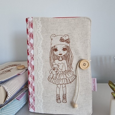 Capa de tecido bege com estampa de boneca e botão de madeira