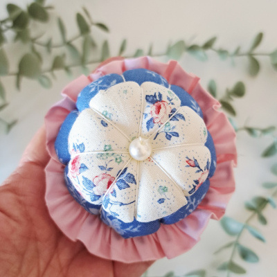 Alfineteiro de tecido floral azul e branco com borda rosa segurado por mão