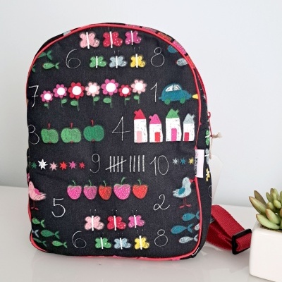 mochila pequena preta com padrão colorido e fecho vermelho