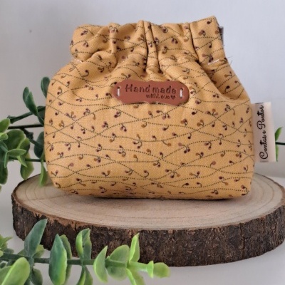 Bolsa artesanal amarela com padrão floral sobre base de madeira com plantas verdes