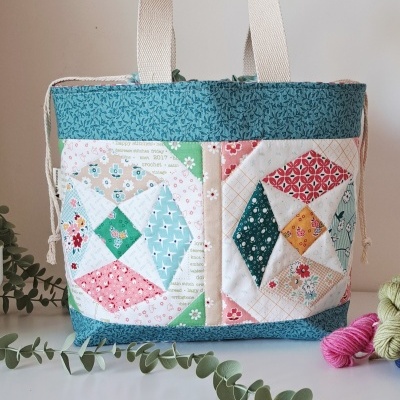 Saco de tecido patchwork com padrões coloridos e alças largas sobre mesa branca