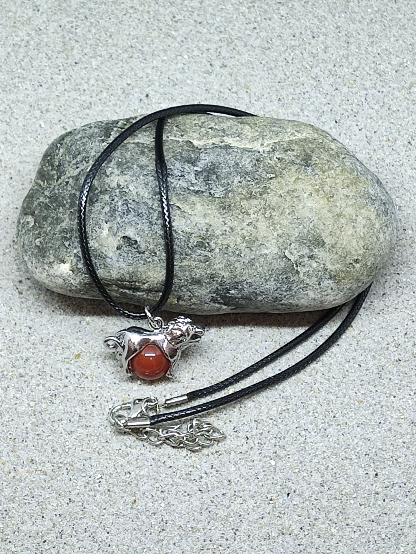 Colar com pendente de cão metálico e pedra vermelha sobre pedra cinza e areia
