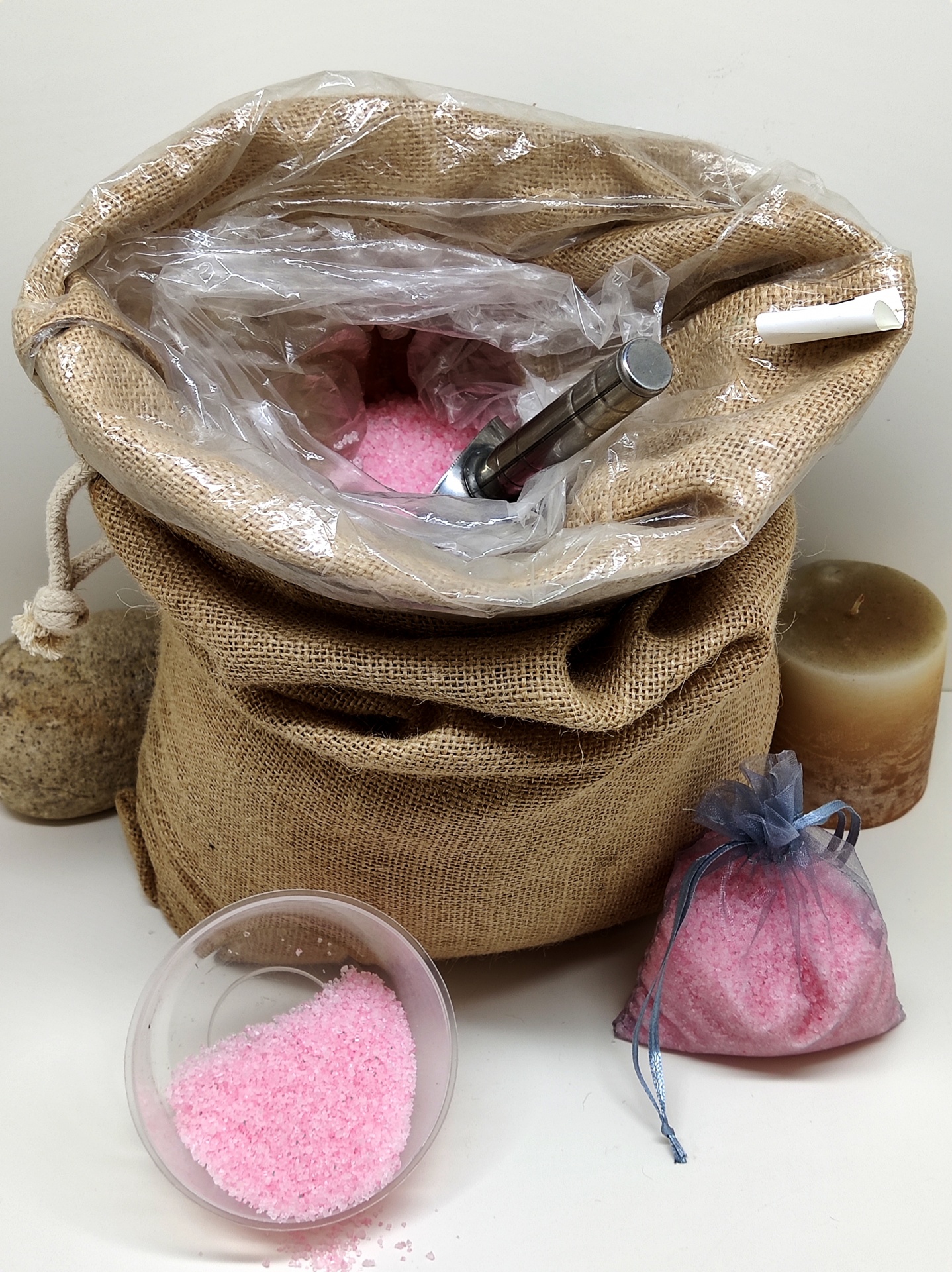 Saco de juta com sal grosso cor-de-rosa, colher metálica, saco de organza com sal, tigela com sal, vela castanha e pedra pendurada