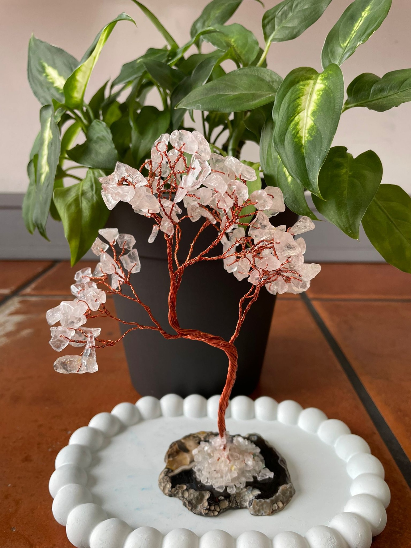 Árvore decorativa de arame e cristais com base de geodo num prato branco em mesa de azulejos