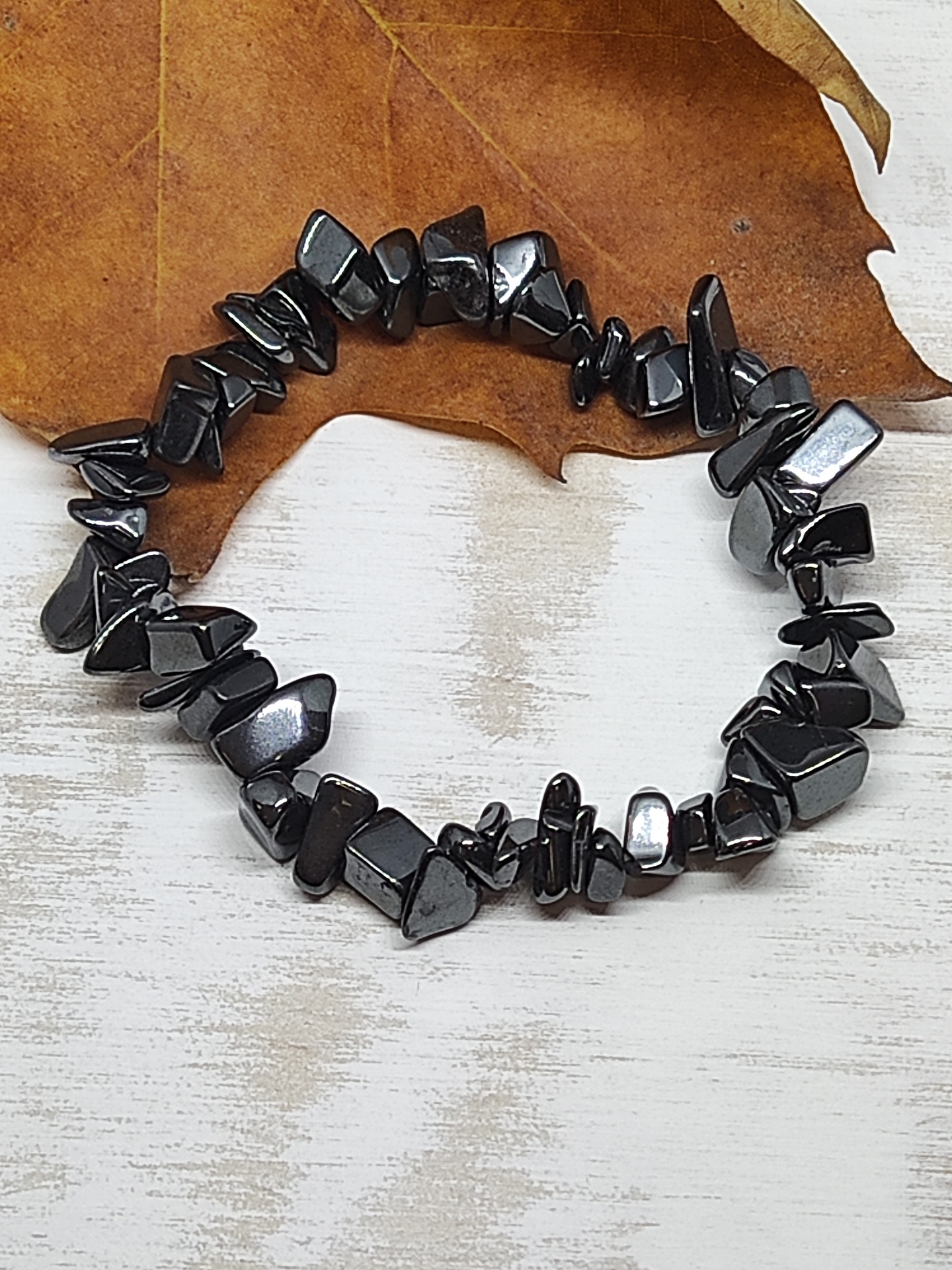 Pulseira de pedras pretas polidas sobre superfície branca com folha seca castanha ao fundo