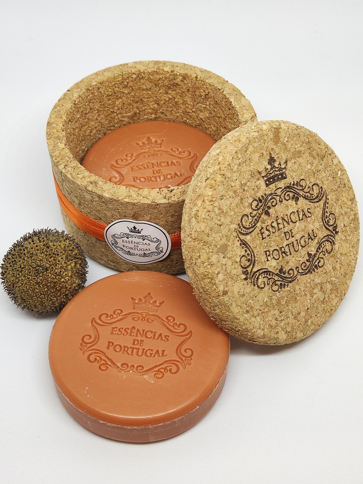 Sabonete laranja redondo com embalagem de cortiça e planta seca ao lado