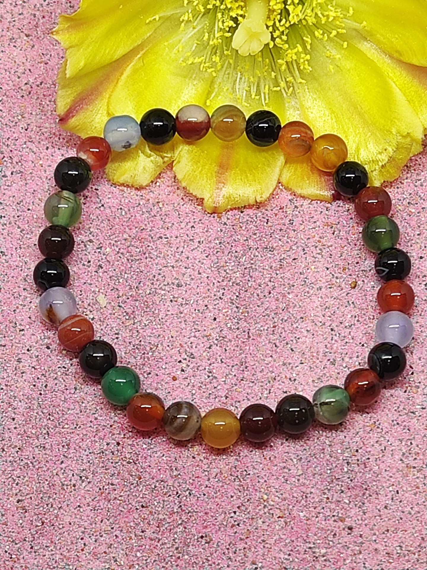 Pulseira colorida com contas redondas sobre fundo rosa e flor amarela