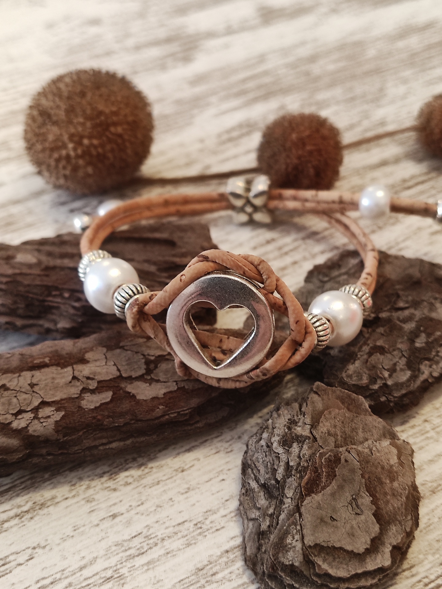 Pulseira de cortiça com fecho em forma de coração em fundo de madeira e elementos naturais