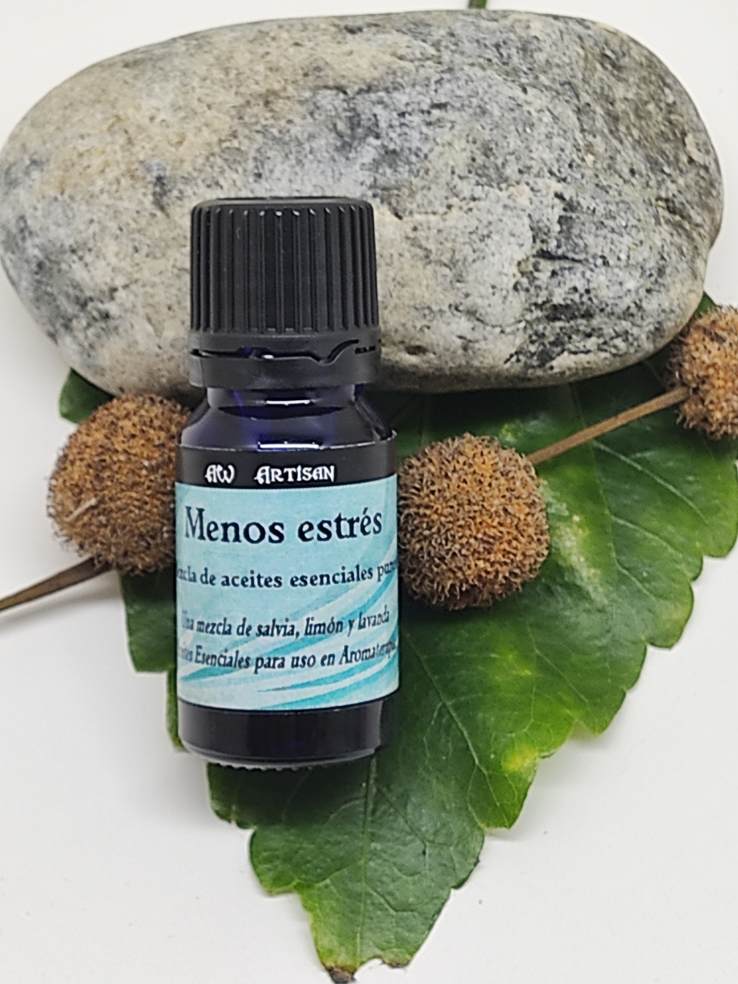 Frasco azul escuro de óleo essencial com rótulo azul claro sobre folhas e pedra