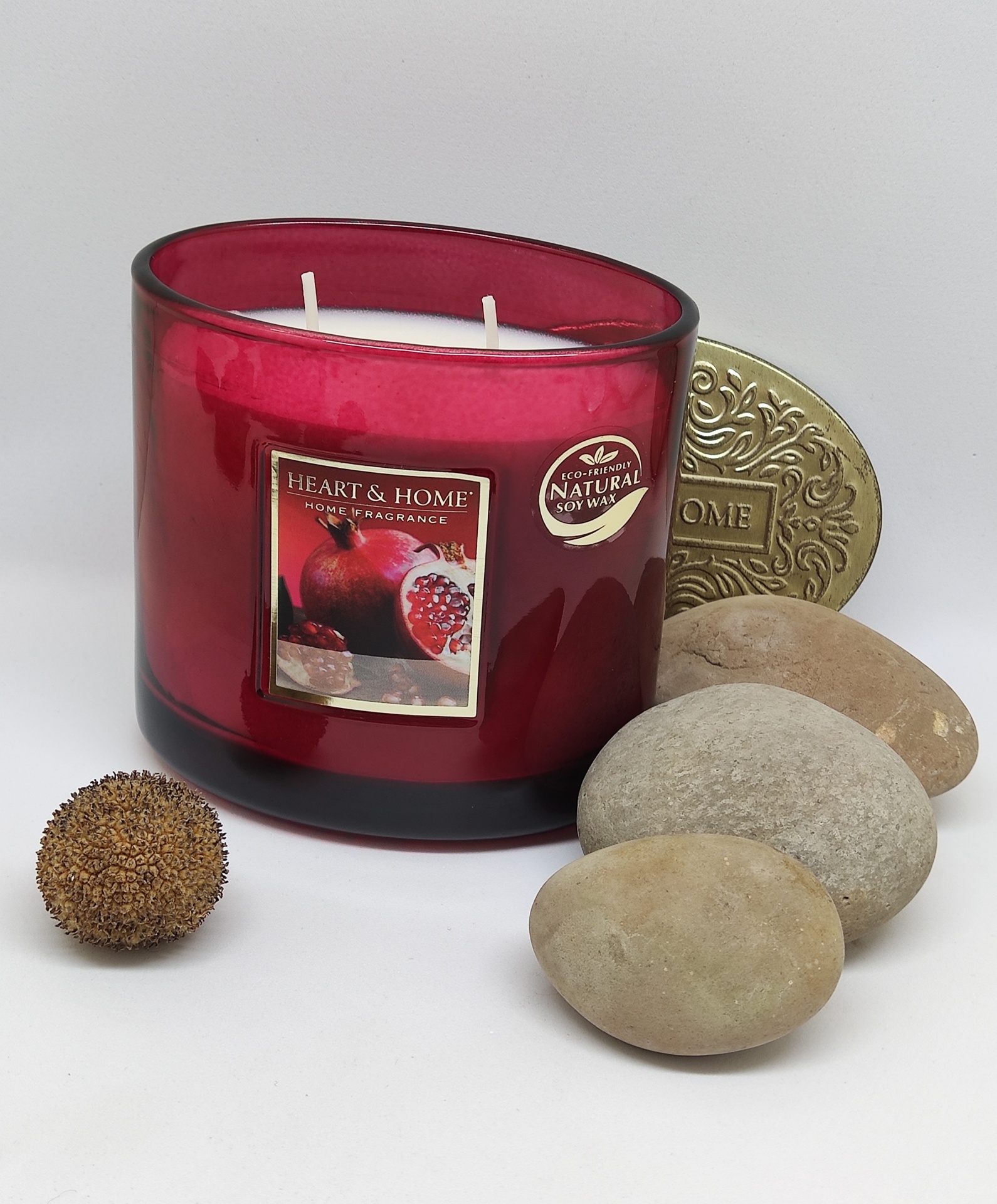 Vela aromática Heart & Home em copo de vidro vermelho rodeada de pedras