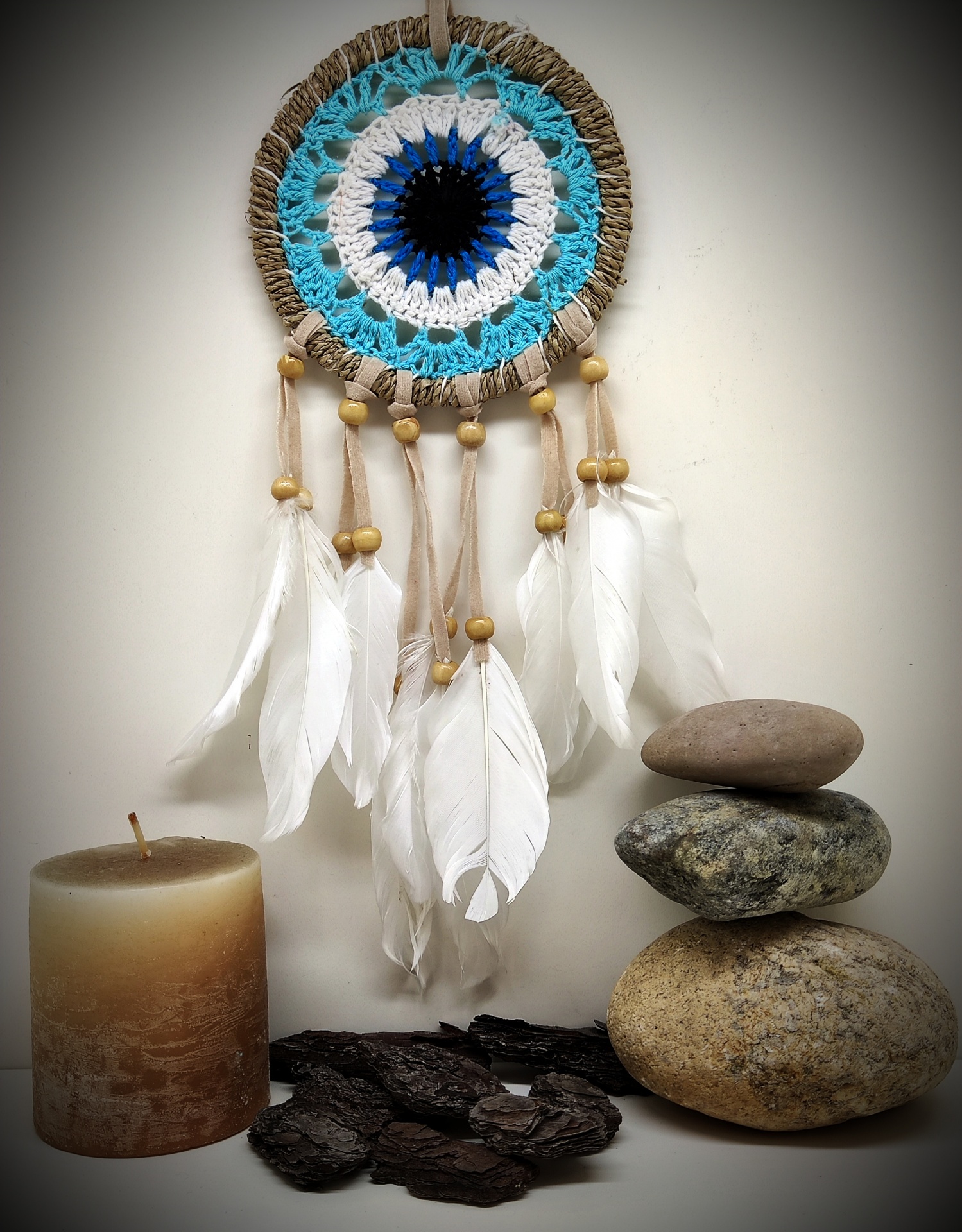 Filtro dos sonhos azul e branco com penas, vela, pedras e madeira