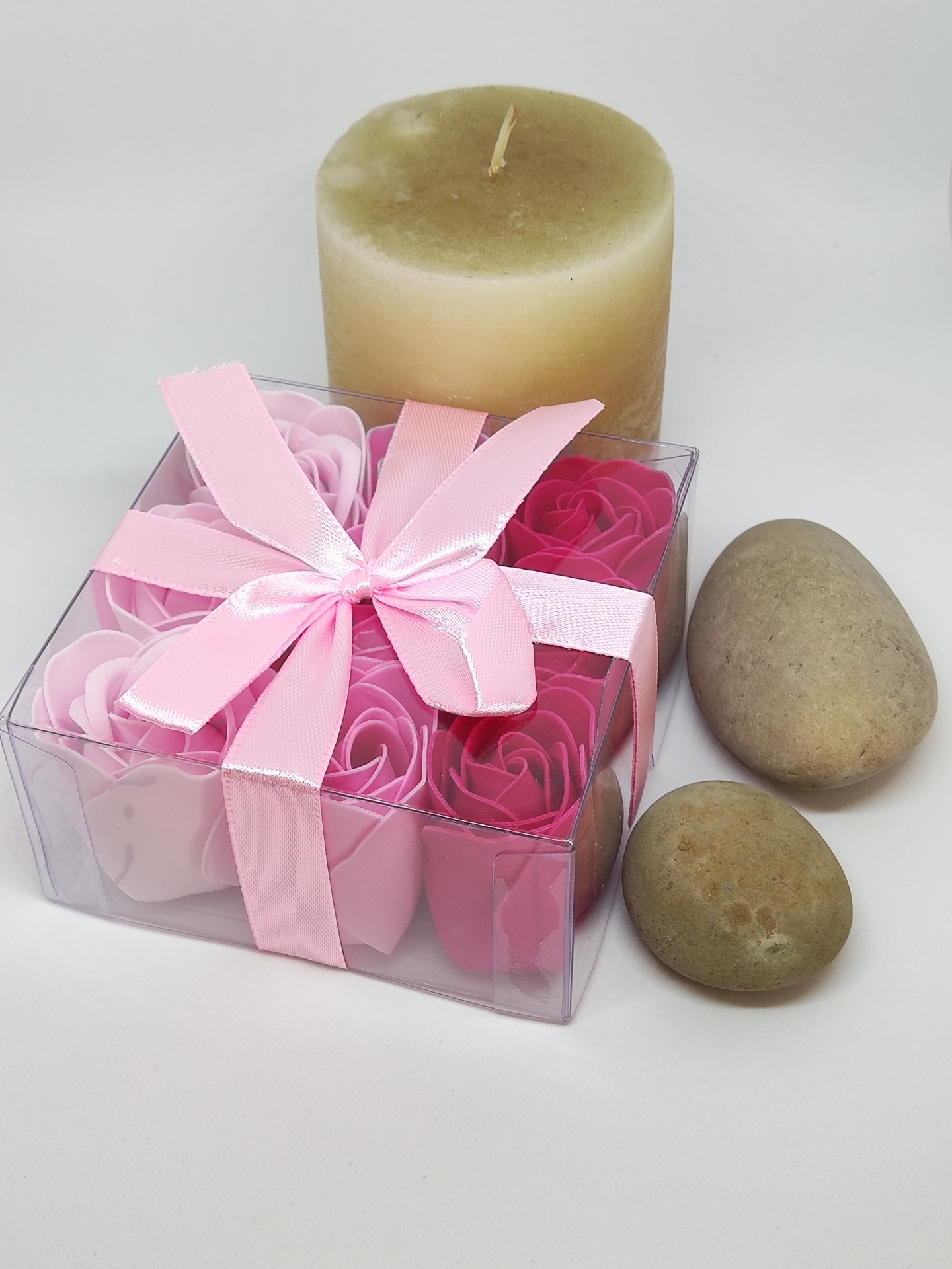 Caixa transparente com flores de sabão rosa, vela bege e duas pedras
