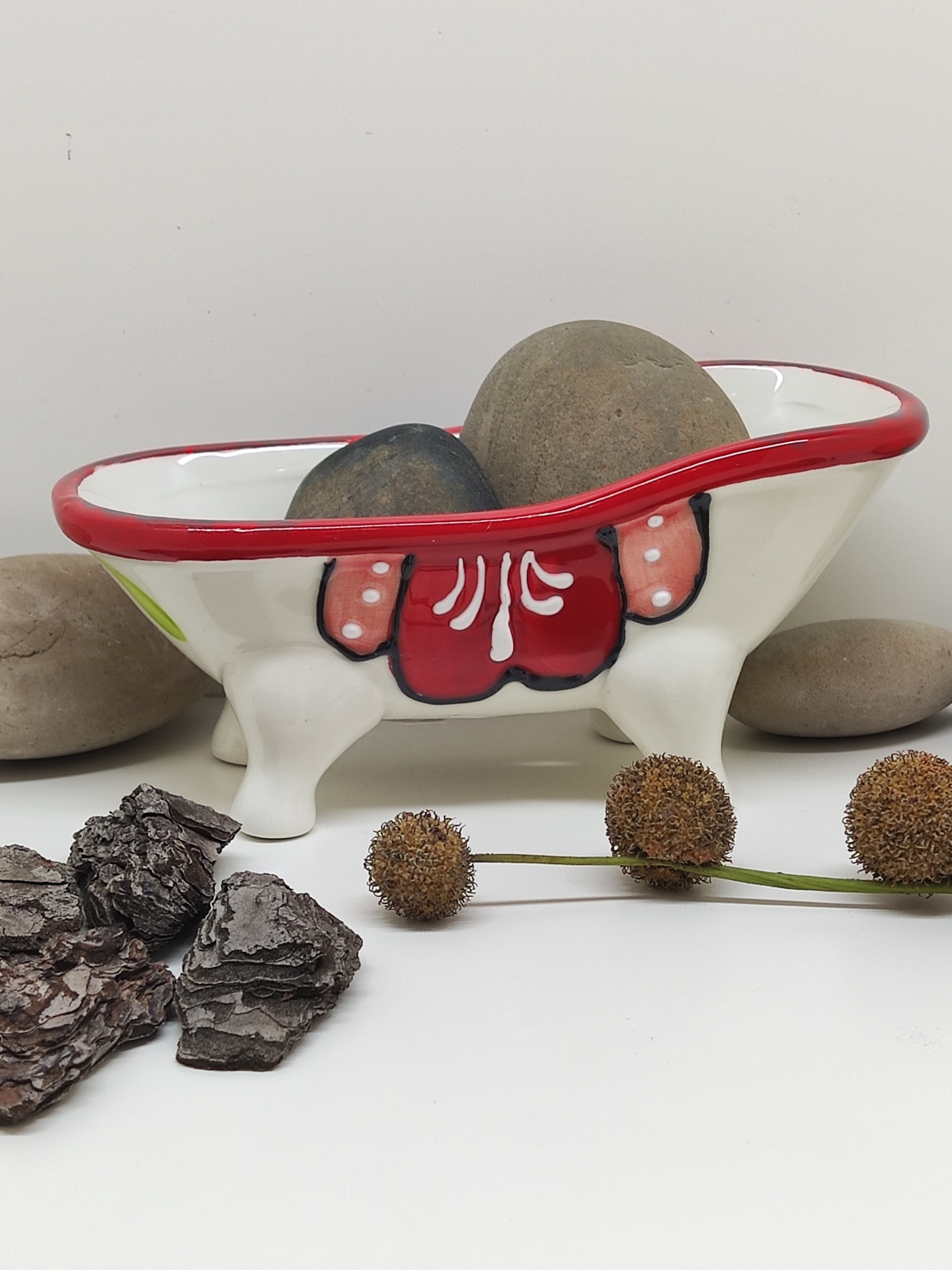 Banheira decorativa cerâmica branca com rebordo vermelho contendo pedras e decoração vermelha e rosa