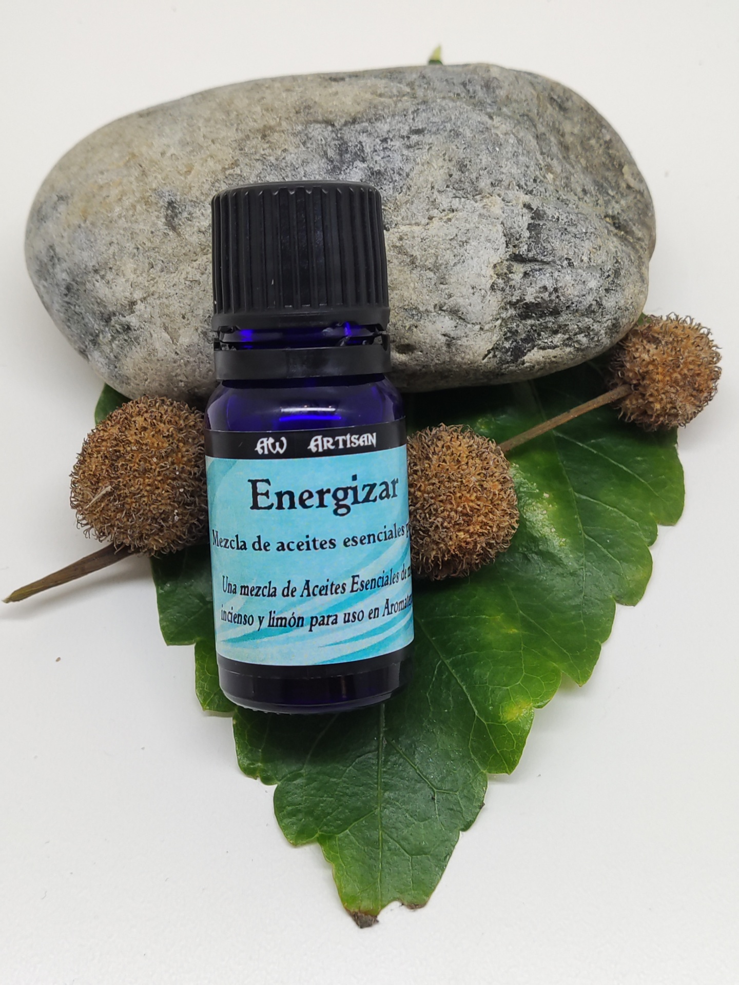 Frasco azul de óleos essenciais chamado Energizar sobre folha e pedras