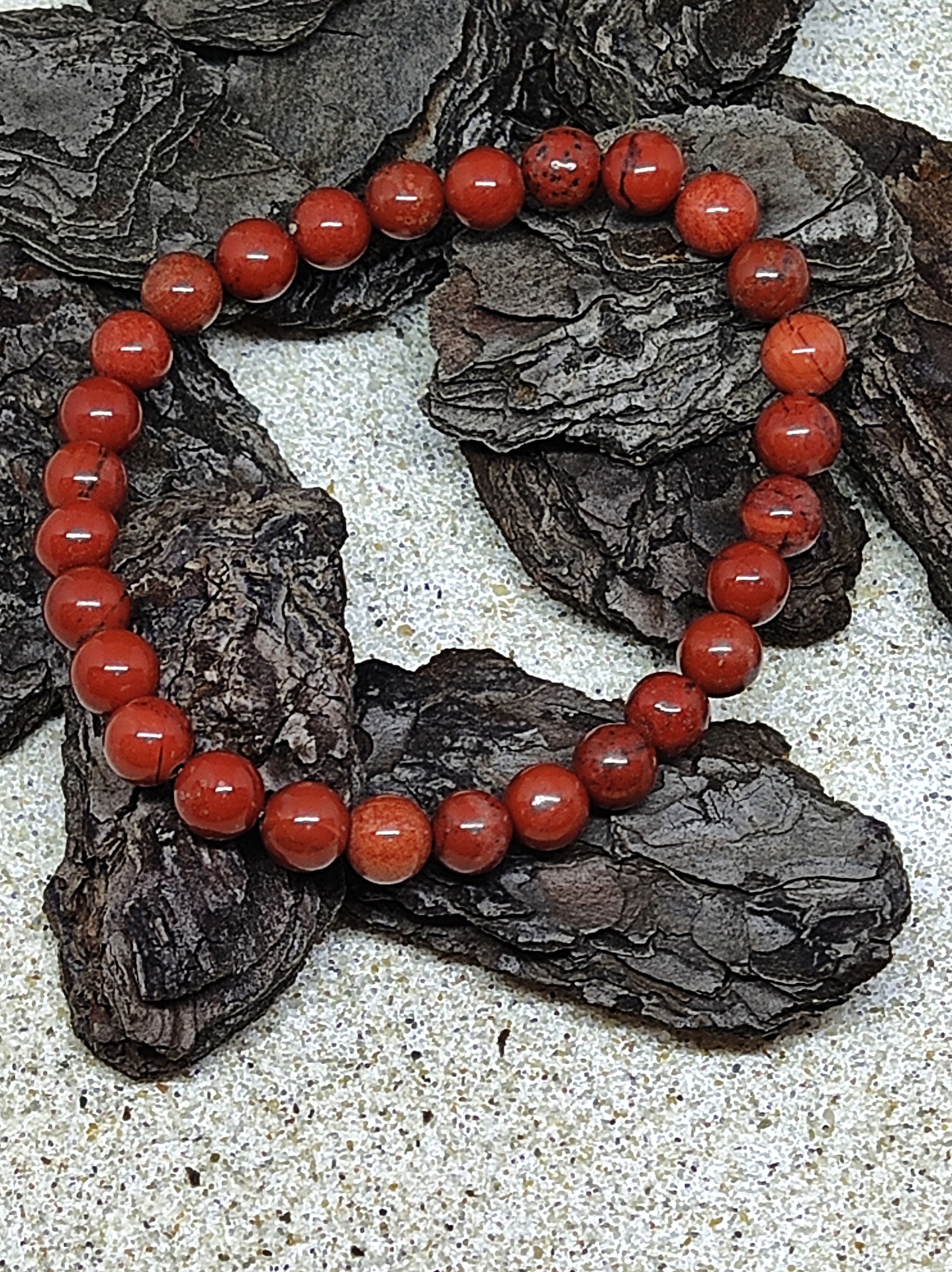 Pulseira elástica de contas de madeira castanho avermelhado sobre cascas de árvore secas.