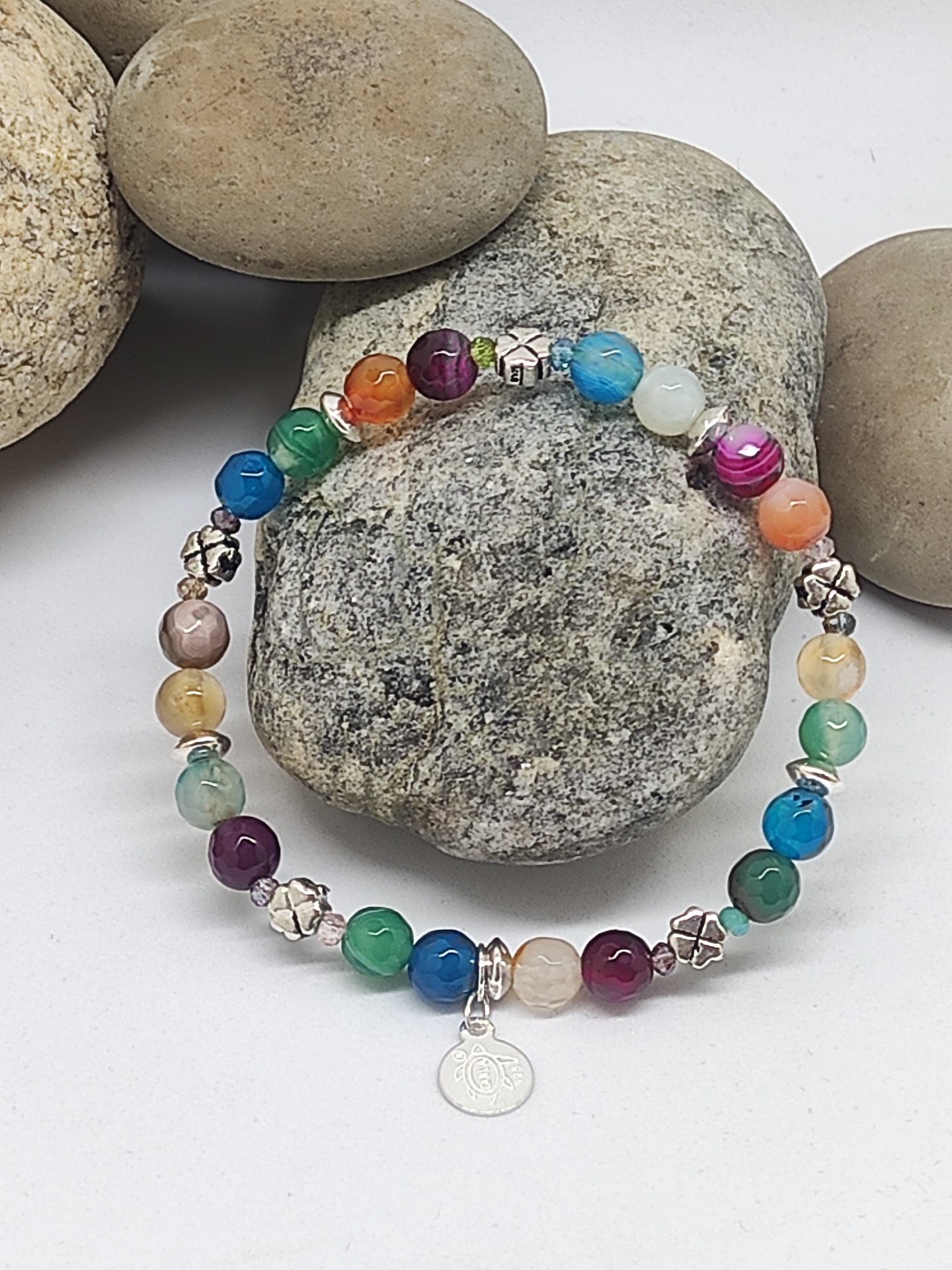 Pulseira elástica multicolorida com contas redondas e pendente OM sobre pedras.