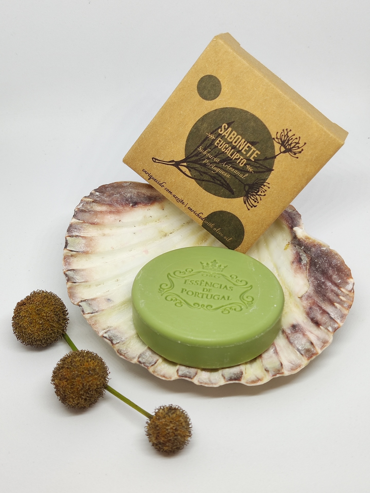Sabonete verde em concha com embalagem de cartão castanho rotulada e flores secas ao lado