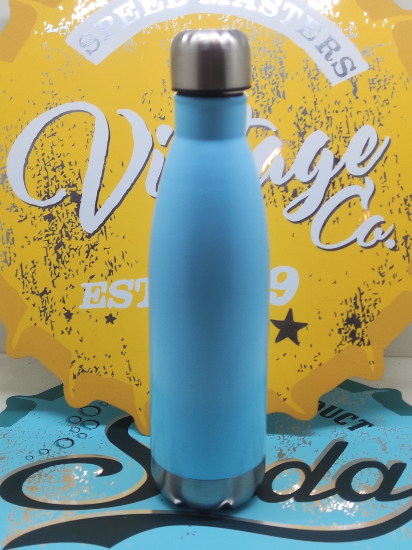 Garrafa térmica azul clara com tampa inox sobre fundo amarelo e azul com textos decorativos