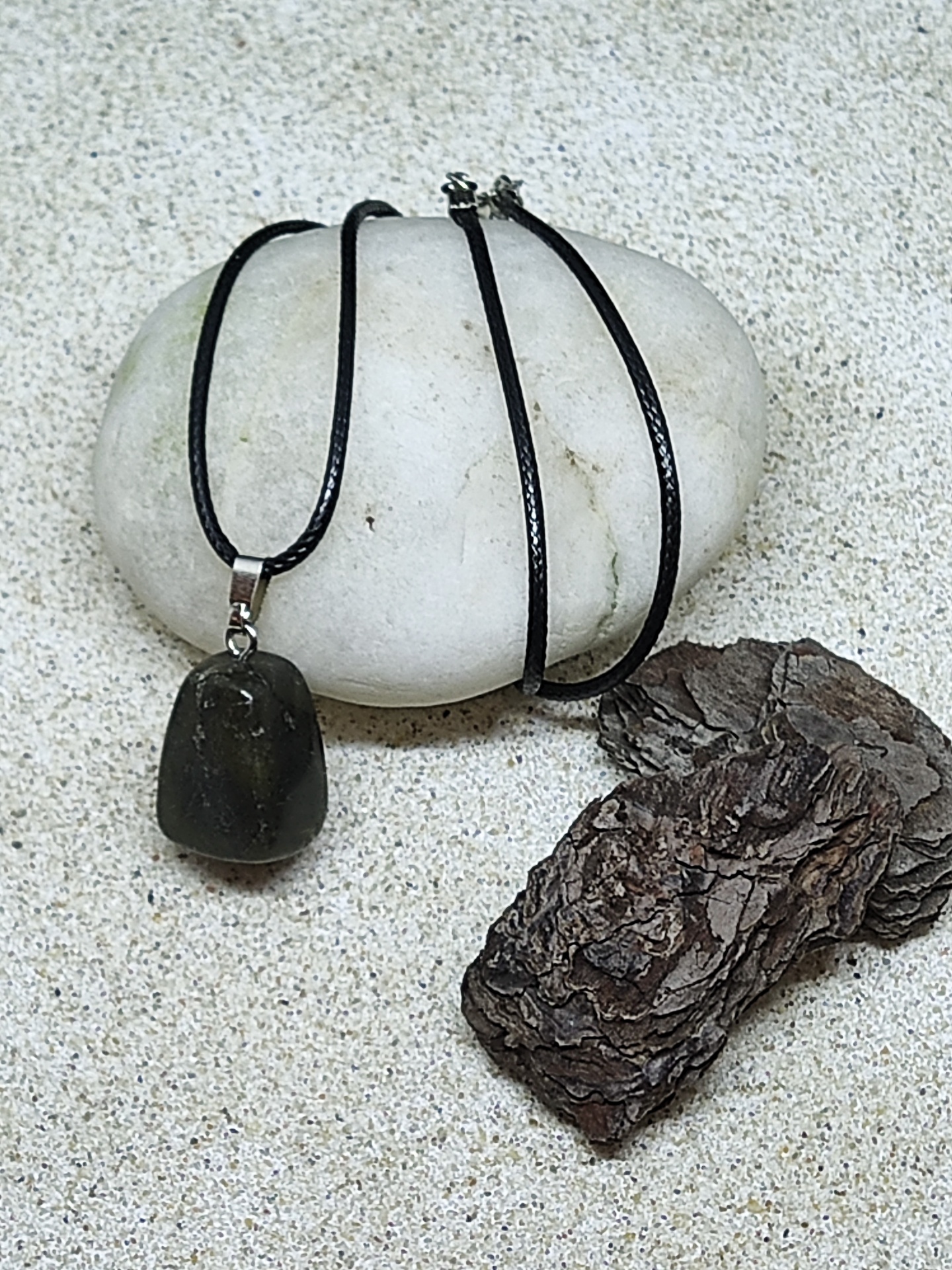 Colar com pendente de pedra preta sobre pedra branca e casca de árvore na areia
