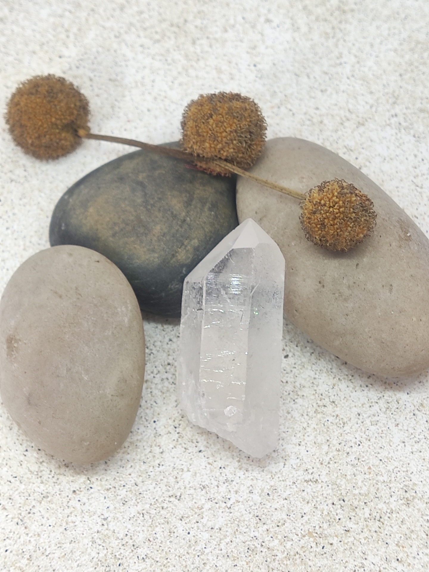 Três pedras lisas, galho seco com bolas castanhas e cristal transparente