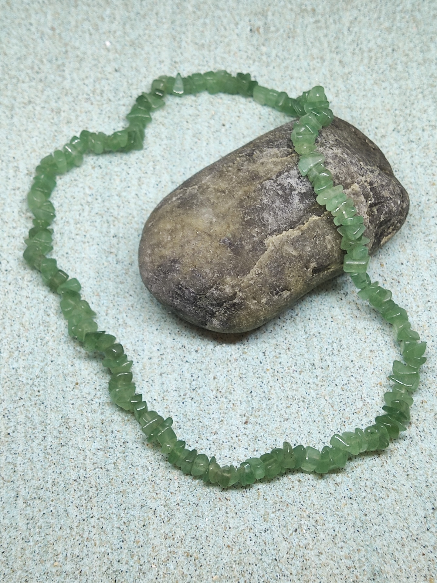 Colar de pedras verdes sobre superfície clara ao lado de pedra maior